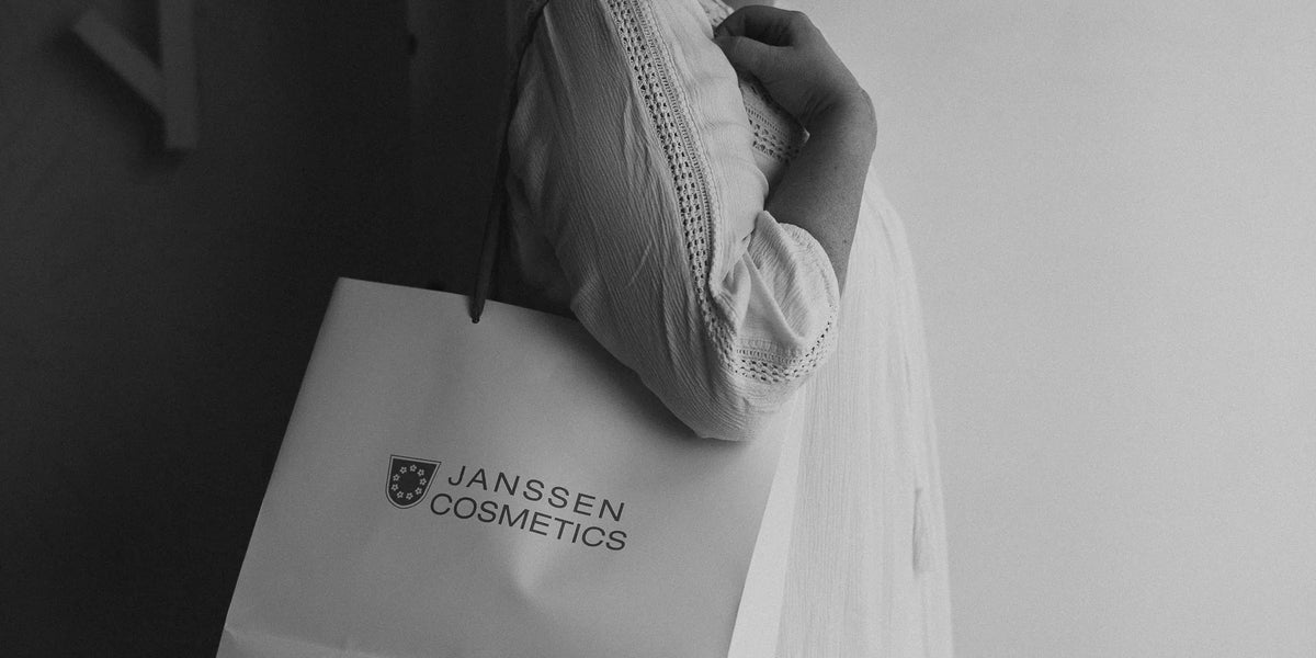 Mustavalkoinen lähikuva, jossa naisen olkapäällä Janssen Cosmetics lahjakassi