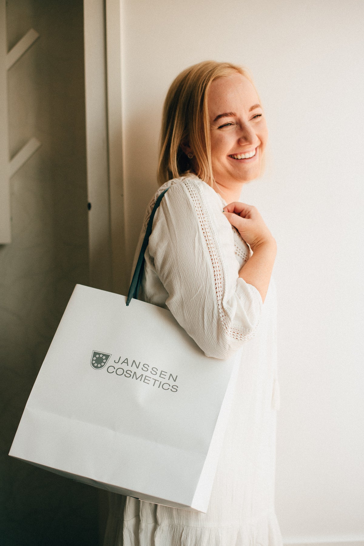Hymyilevä nainen jonka olalla Janssen Cosmeticsin vaalea lahjakassi.